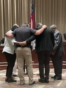 A group of people praying in a council meeting.