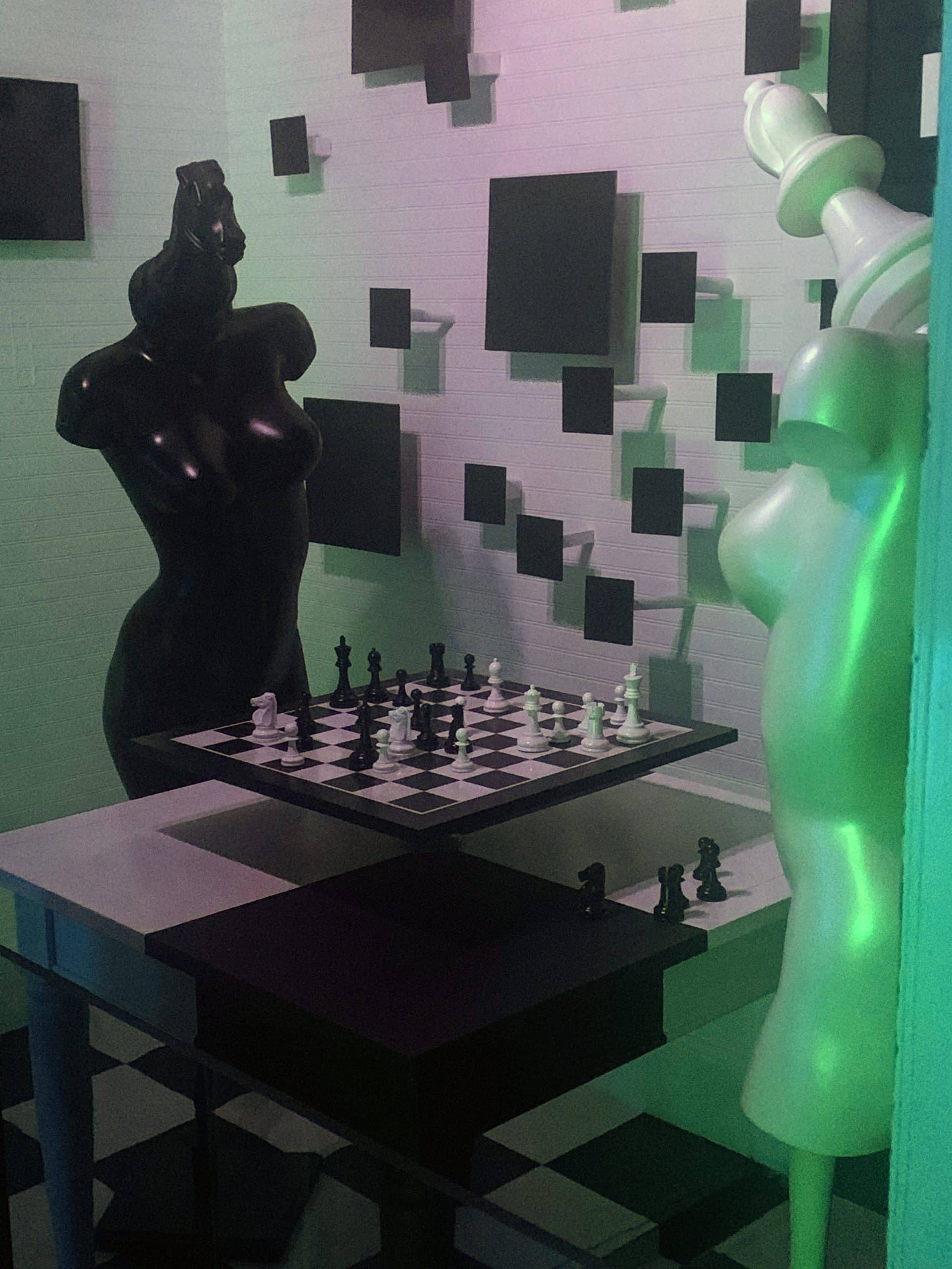 a sculpture of two mannequins, one black, one white, with chess pieces for heads, standing at a chess table.